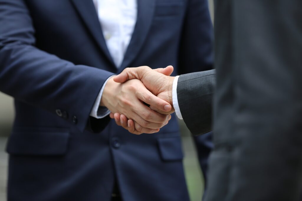 torso and arms of two men in suits shaking hands